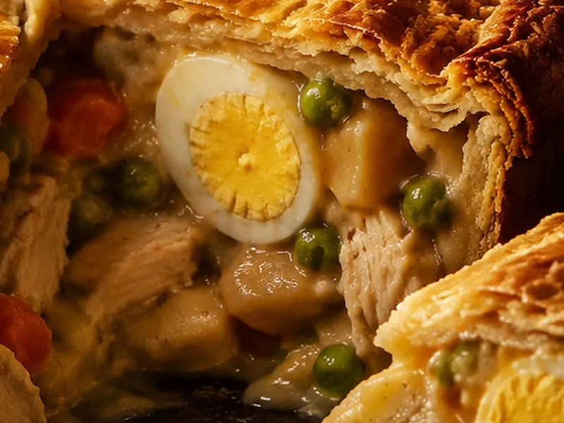 Close-up of a cut chicken pie showing half a hard-boiled egg, chicken, potato, peas and carrot in creamy gravy